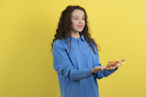 Photo of beautiful young girl giving piece of pizza on yellow background. High quality photo - Valokuva, kuva
