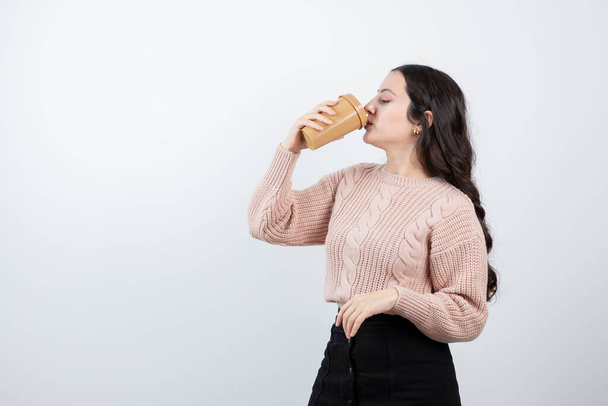 Retrato de menina bonita bebendo de um copo contra a parede branca. Foto de alta qualidade - Foto, Imagem