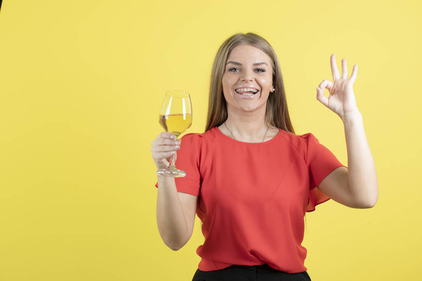Φωτογραφία μιας όμορφης γυναίκας που κρατάει ένα ποτήρι κρασί και δείχνει μια καλή χειρονομία. Υψηλής ποιότητας φωτογραφία - Φωτογραφία, εικόνα