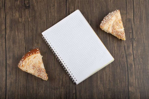 Egy szelet pite kókuszreszelékkel és fehér jegyzetfüzettel az asztalon. Kiváló minőségű fénykép - Fotó, kép