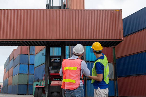 Industrial worker works with co-worker at overseas shipping container yard - Foto, imagen