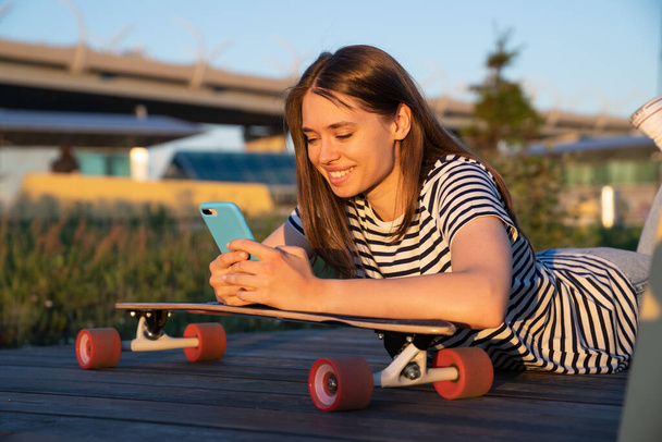 Happy skateboarder girl hold smartphone messaging use mobile 5g internet outdoors for social media - Foto, Bild