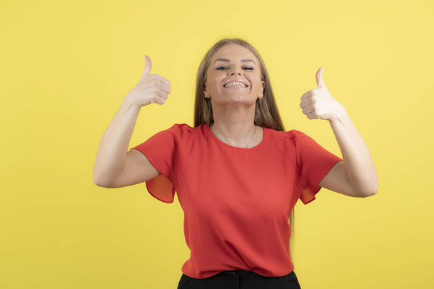 Photo of a young woman with wide smile showing thumbs up on yellow wall . High quality photo - Foto, Bild