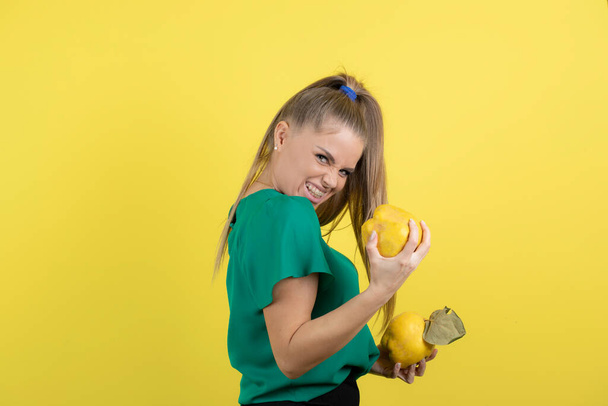 Portret van jonge vrouw in groene top met rijpe kweeperen op haar beide handen. Hoge kwaliteit foto - Foto, afbeelding
