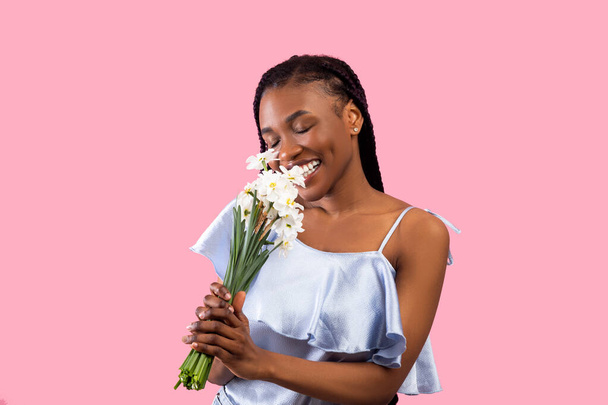 Millennial musta nainen haisee nippu narsisseja vaaleanpunainen studio tausta - Valokuva, kuva