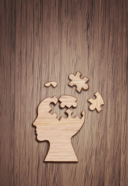 Menselijk hoofd silhouet met een puzzel stuk uitgesneden op de houten ondergrond, symbool van de geestelijke gezondheid. - Foto, afbeelding