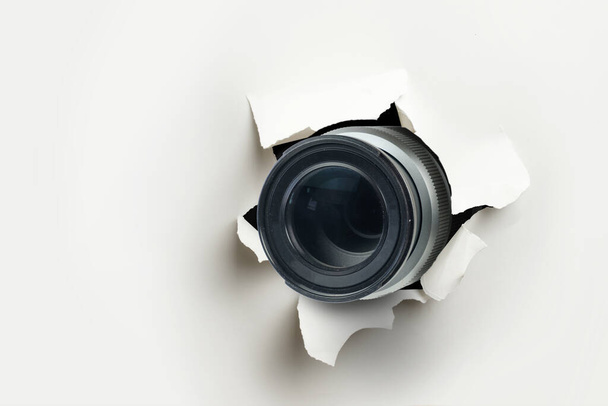 Έννοια του παπαράτσι ή κρυμμένη κάμερα, φακός κάμερα κοιτάζει μέσα από μια τρύπα στο λευκό τοίχο από χαρτί - Φωτογραφία, εικόνα