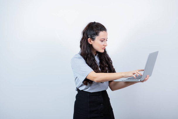 白い背景にラップトップコンピュータを持っている若いブルネットの女の子の肖像画。高品質の写真 - 写真・画像