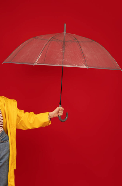 Woman in raincoat holding transparent umbrella against red backgroud, studio shot, crop. Autumn accessories concept - Foto, Imagem