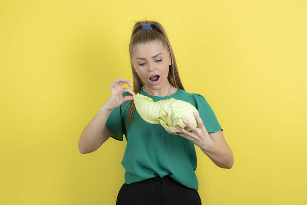 Portrait of lovely girl looking at green cabbage over yellow wall. High quality photo - Photo, Image