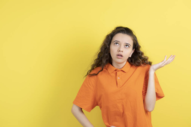 Image of curly teen girl in orange t-shirt posing on yellow background. High quality photo - Photo, image