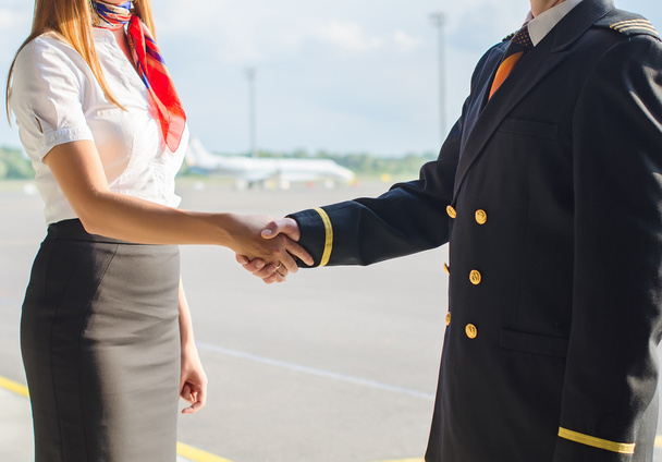 piloot en stewardess schudden handen op vliegveld achtergrond. - Foto, afbeelding