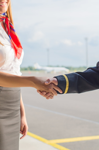 piloot en stewardess schudden handen op vliegveld achtergrond. - Foto, afbeelding