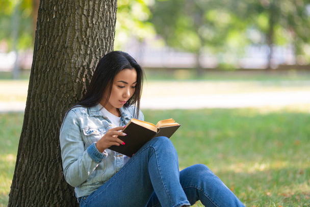 Donna asiatica con un libro sotto l'albero nel parco. Il concetto di disintossicazione digitale. - Foto, immagini