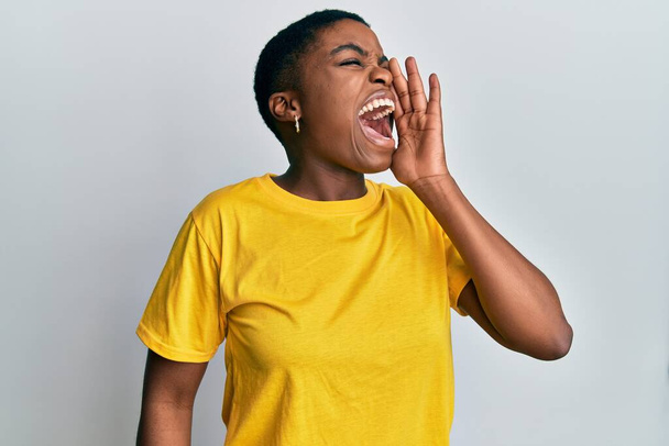 若いアフリカ系アメリカ人の女性は、カジュアルな黄色のtシャツを着て大声で叫び、口の上に手で大声で叫ぶ。コミュニケーションの概念.  - 写真・画像