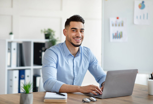 Vonzó fiatal arab üzletember, aki laptopot használ az íróasztalánál az otthoni irodában. - Fotó, kép