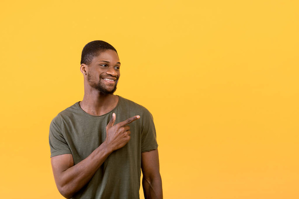 Positiver schwarzer Typ lächelt und zeigt zur Seite auf freien Raum, isoliert über gelbem Studiohintergrund, Banner - Foto, Bild