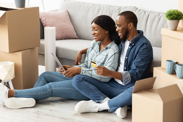 Gli sposi neri felici che scelgono la mobilia in linea con la compressa digitale e la carta di credito - Foto, immagini