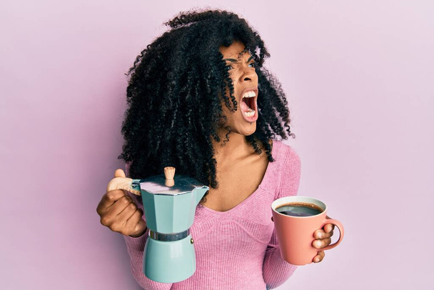 Afrikai amerikai nő afro hajjal olasz kávét iszik dühösen és őrülten sikoltozva frusztráltan és dühösen, dühösen kiabálva. düh és agresszív koncepció.  - Fotó, kép