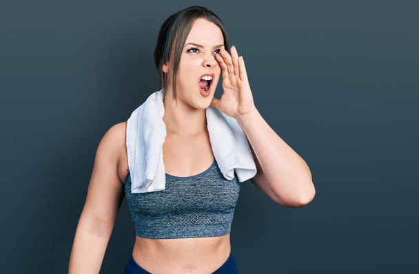 Jong Latijns-Amerikaans meisje draagt sportkleding en handdoek schreeuwend en schreeuwend luid naar zij met hand op mond. communicatieconcept.  - Foto, afbeelding
