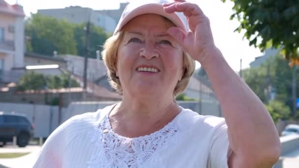Portret van een gelukkige vrouw met pensioengerechtigde leeftijd, een gepensioneerde corrigeert een pet van de zon - Video