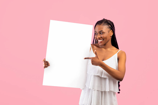 Радостная черная женщина с афро пучками, указывающими на пустой баннер с пространством для дизайна на розовом фоне - Фото, изображение