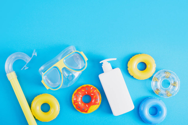 set for beach recreation and diving, sun cream or sun protection and toy inflatable circles on a blue background, mock up blank white cream bottle - Fotoğraf, Görsel