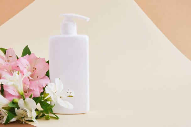 flowers and white blank bottle with dispenser for soap or cosmetics on beige background Natural cosmetic packaging. mock up beauty product concept. - Foto, immagini