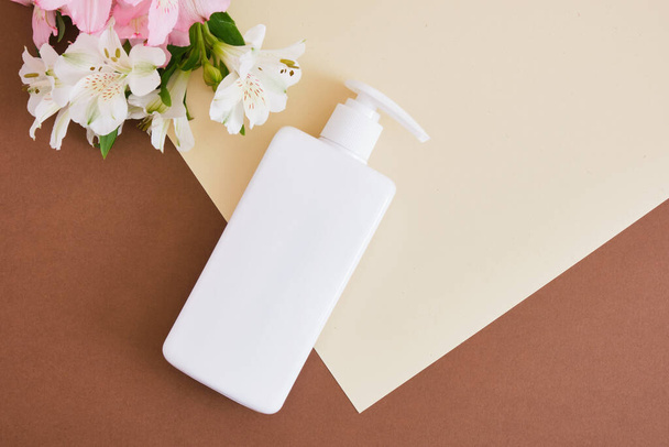 flowers and white blank mock up bottle with dispenser for soap or cosmetics on beige brown background Natural cosmetic packaging. mock up beauty product concept. - Zdjęcie, obraz