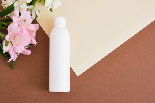 lily flowers and blank mock up bottle with green cosmetics gel or lotion on beige brown background Natural cosmetic packaging. mock up beauty product concept. - Photo, Image