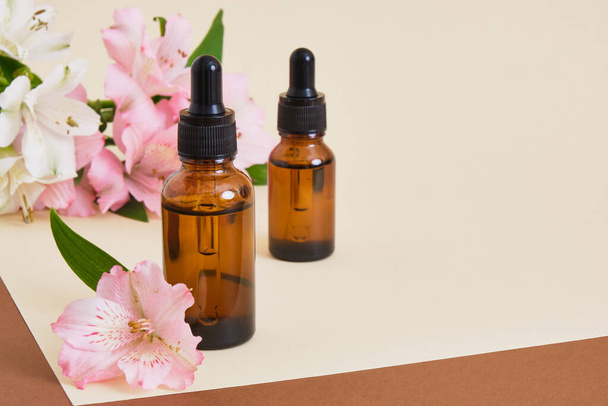 Amber glass bottles a beige brown background with a lily flowers. copy space. Cosmetic, skin care concept, gentle care, natural body care set top view - Foto, imagen