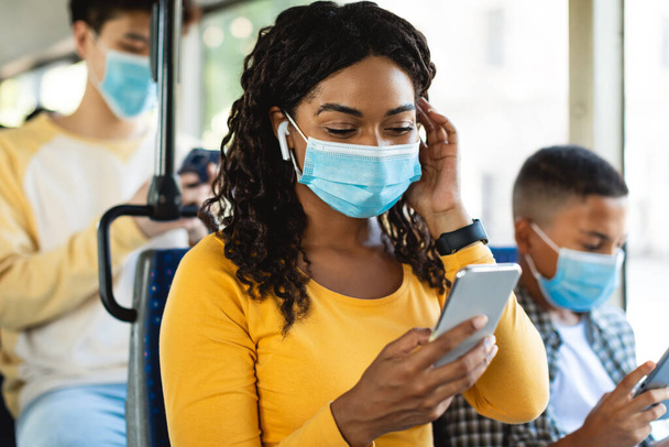 Smiling black woman in mask listening music in bus - Photo, image