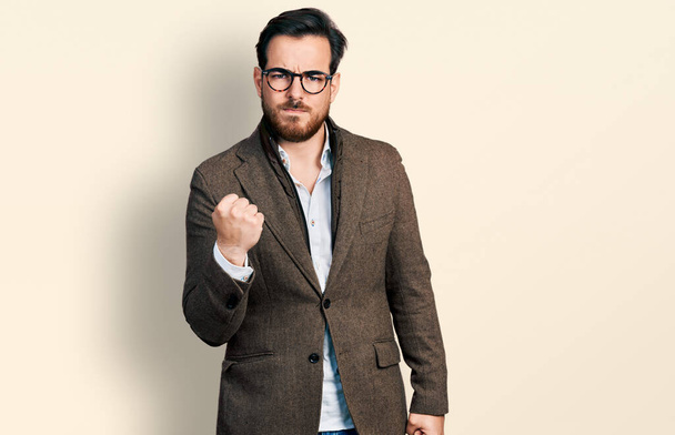 Young hispanic man wearing business jacket and glasses angry and mad raising fist frustrated and furious while shouting with anger. rage and aggressive concept.  - Valokuva, kuva
