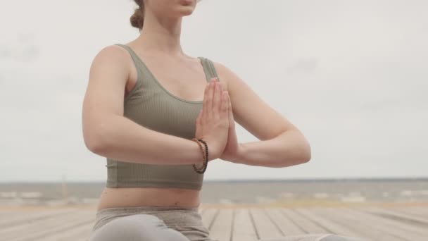 Mittelteil-Slowmo-Aufnahme einer jungen Frau, die tief atmet und in Lotus-Pose mit betenden Händen meditiert, während ihr eine Yoga-Trainerin hilft - Filmmaterial, Video