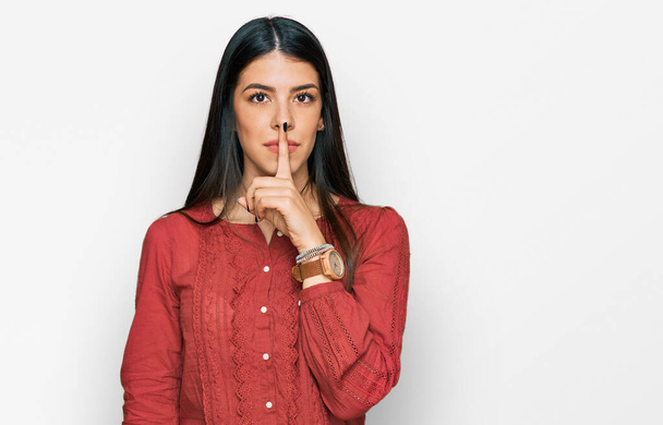 Молода іспаномовна жінка в повсякденному одязі просить мовчати з пальцем на губах. тиша і таємна концепція
.  - Фото, зображення