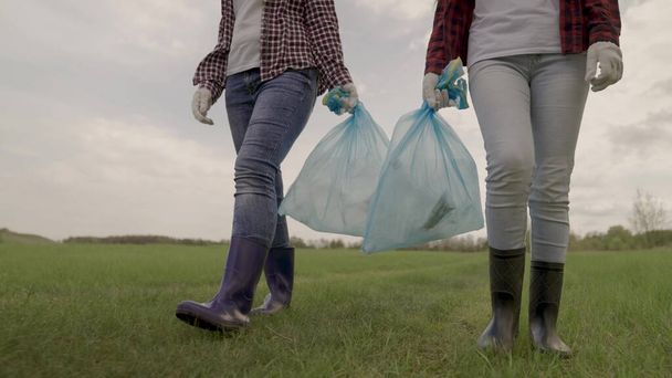 волонтеры собирают мусор в мешки для мусора, защищают природу от загрязнения, коллективную работу по утилизации отходов, благотворительную деятельность активистов, чистую природу, экологию, людей в резиновых сапогах - Фото, изображение