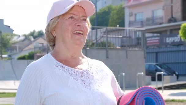 Sorridente anziana donna sportiva cammina con fiducia nel parco del mattino  - Filmati, video