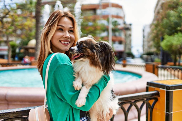 Jeune fille caucasienne souriant heureux tenant chien à la ville. - Photo, image
