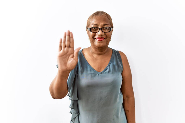 Mature hispanic woman wearing glasses standing over isolated background waiving saying hello happy and smiling, friendly welcome gesture  - Photo, Image