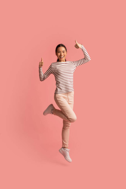 Cheerful Asian Woman Showing Thumbs Up At Camera While Jumping In Air - Φωτογραφία, εικόνα