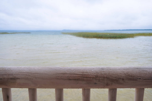 Wooden fence on a storm lake background. Hewn pine log in the rain. - Photo, Image