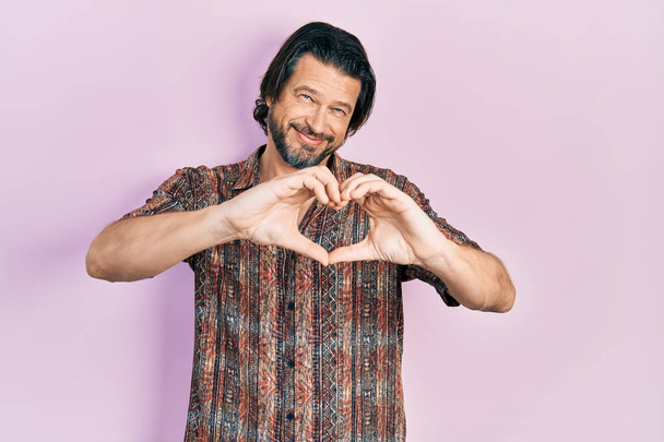 Középkorú kaukázusi férfi alkalmi ruhát visel mosolyogva a szerelemben csinál szív szimbólum alakú kezekkel. romantikus koncepció.  - Fotó, kép