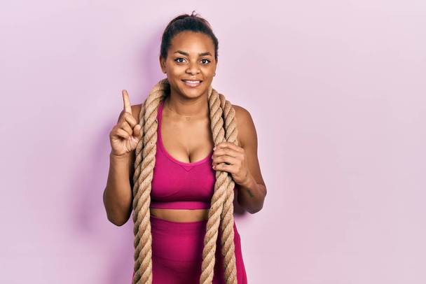 jong afrikaans amerikaans meisje training met strijd touw glimlachen met een idee of vraag wijzend vinger met gelukkig gezicht, nummer een  - Foto, afbeelding