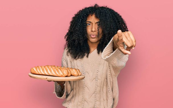 Junge Afroamerikanerin hält Tablett mit Brot und zeigt mit dem Finger in die Kamera und zu dir, selbstbewusste Geste, die ernst wirkt  - Foto, Bild