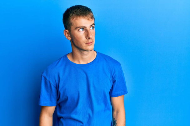 Молодой кавказский мужчина в обычной голубой футболке, улыбаясь, смотрит в сторону и думает:.  - Фото, изображение