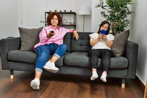 Mature mother and down syndrome daughter at home watching television and using smartphone - Foto, immagini