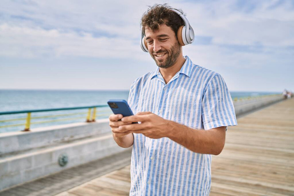 Young hispanic man smiling happy listening to music at the promenade. - Фото, зображення