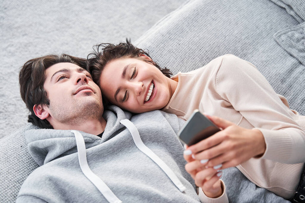 夫婦は家で一緒に時間を過ごし、笑顔でスマートフォンを見て - 写真・画像