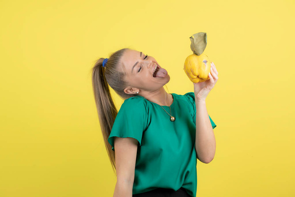 Image d'une jeune femelle mangeant des fruits mûrs de coing sur un mur jaune. Photo de haute qualité - Photo, image