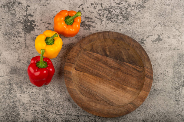 Wooden plate and colorful sweet bell peppers on stone background. High quality photo - Photo, image